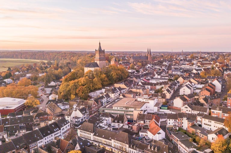 Aerial view of a historic European town with church spires, autumn foliage, and residential buildings at sunset