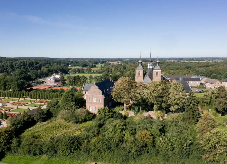 Aerial view of a brick castle with twin towers surrounded by green forest and countryside landscape