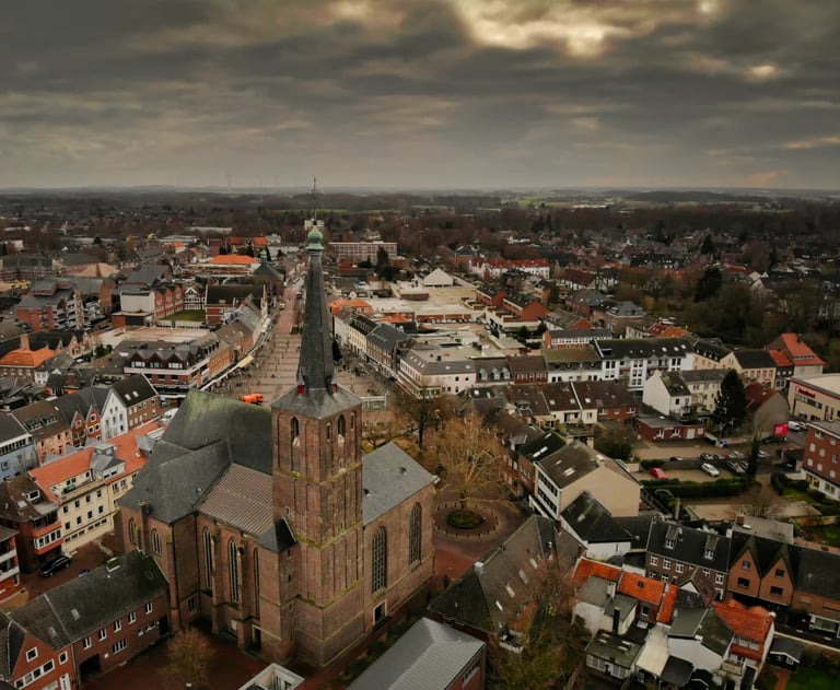 Aerial view of a European city with a prominent brick church, residential buildings, and overcast sky in the background