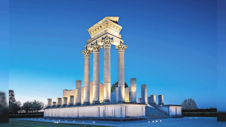 Illuminated classical monument with tall columns and ornate capital against a clear blue sky at dusk